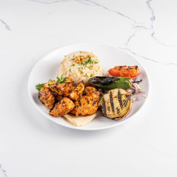 Grilled chicken pieces, rice, grilled vegetables, and pita bread on a white plate.