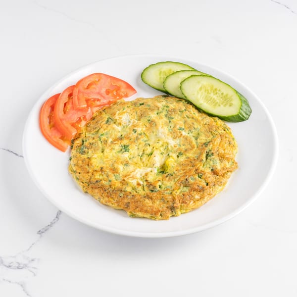 A golden omelet with herbs, served on a white plate with sliced tomatoes and cucumbers.