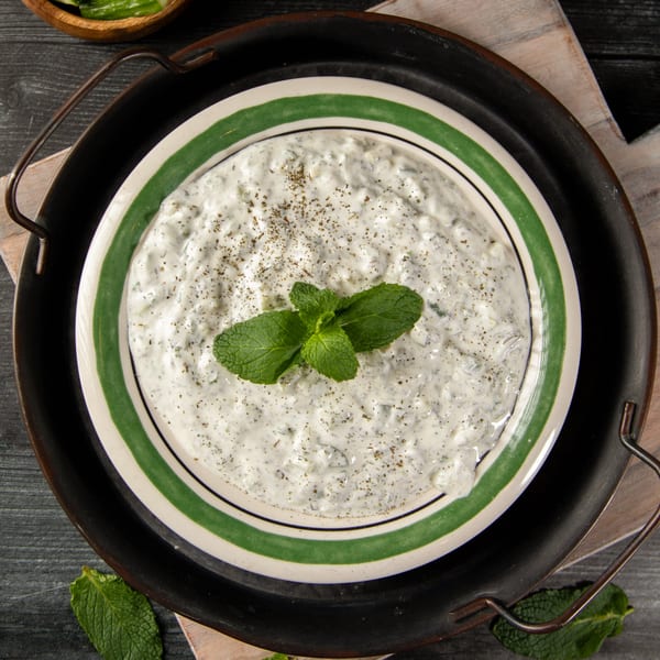 Palestinian yogurt dip, laban ma'a khiar, garnished with mint and spices in a green-striped bowl.