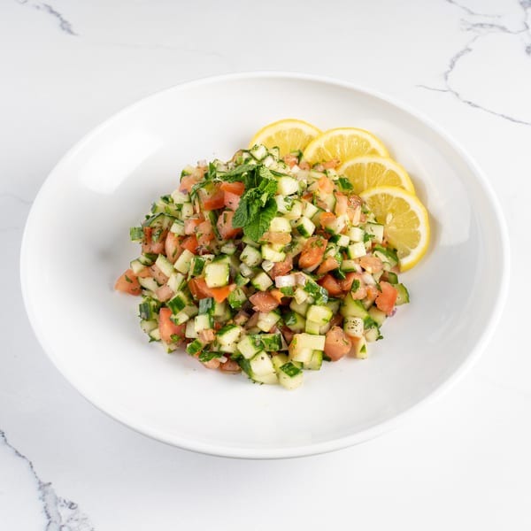 Diced cucumber and tomato salad with fresh mint and lemon slices on a white plate.