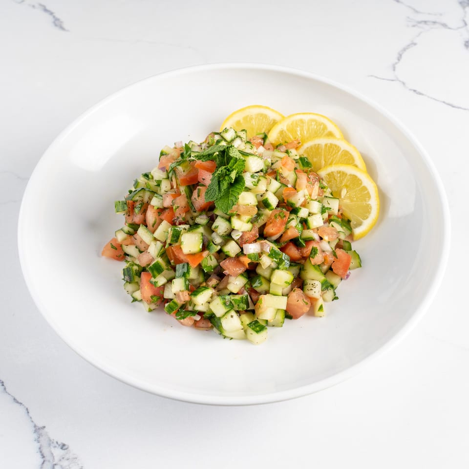 Diced cucumber and tomato salad with fresh mint and lemon slices on a white plate.