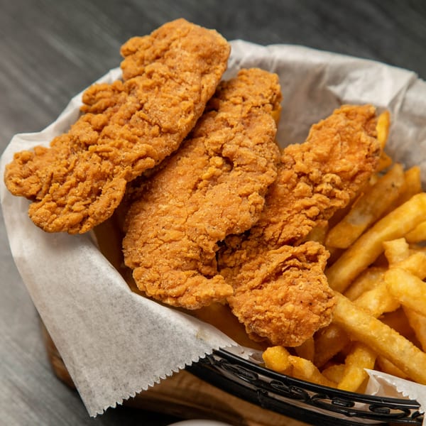 Crispy fried chicken tenders and golden french fries served in a basket lined with white paper.