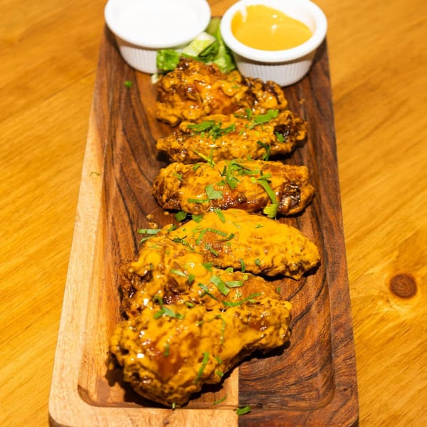 Chicken wings coated in a golden sauce and garnished with herbs, served on a wooden platter with dips.