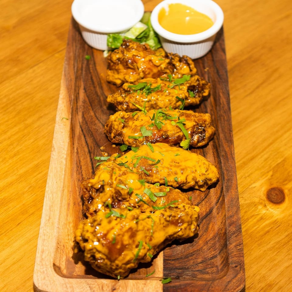 Chicken wings coated in a golden sauce and garnished with herbs, served on a wooden platter.