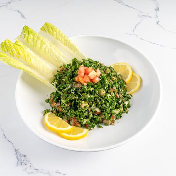A fresh tabbouleh salad with chopped parsley, tomatoes, and lemon wedges on a white plate.