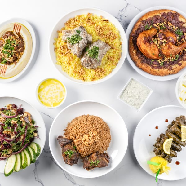 Overhead view of a feast of Middle Eastern dishes, including hummus, rice, chicken, and stuffed grape leaves.
