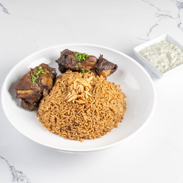 Chicken and rice with almonds in a white bowl, with a side of tzatziki sauce.