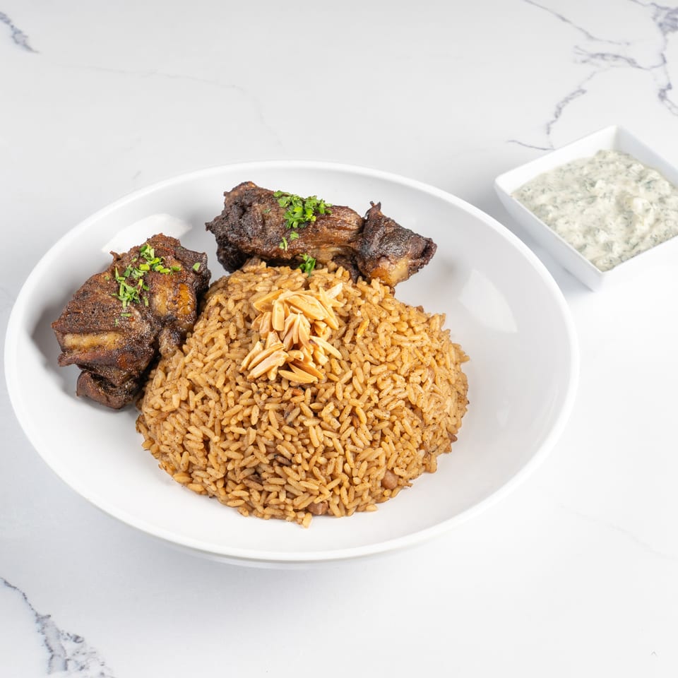 Chicken and rice with almonds in a white bowl, with a side of tzatziki sauce.