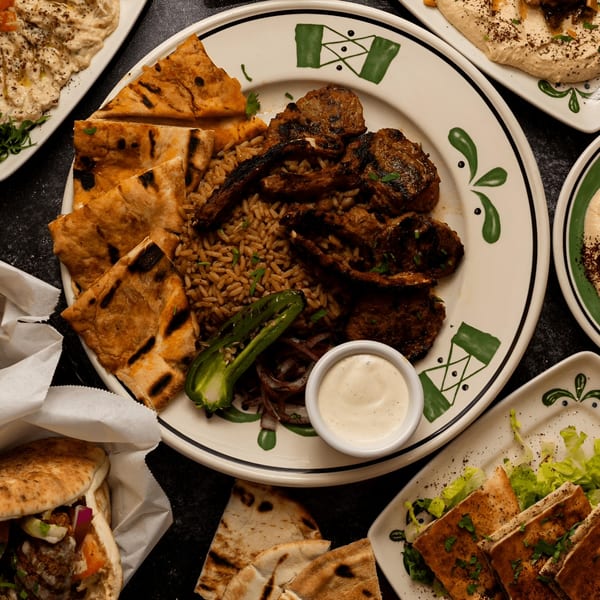 Palestinian lamb chops with rice, grilled peppers, pita bread, and dipping sauce on a decorative plate.