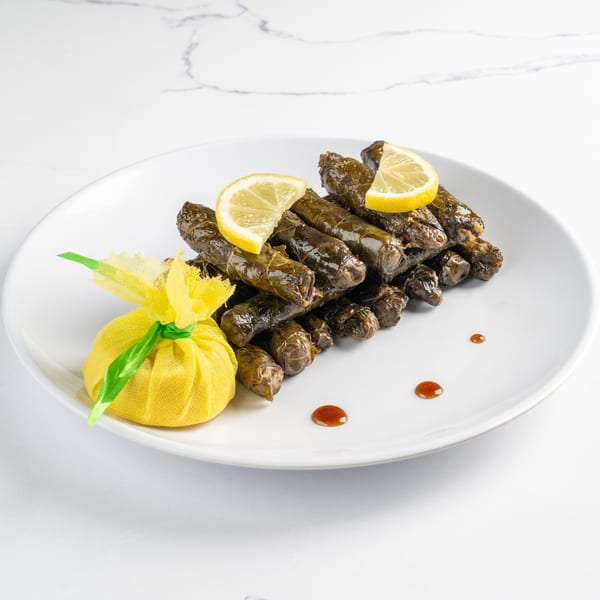 A white plate with a pile of dolmas, lemon wedges, and a yellow mesh pouch.