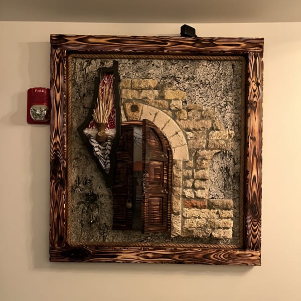 A framed Palestinian art piece depicting an open wooden door in a stone wall, with wheat stalks.
