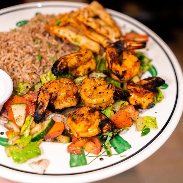 Grilled shrimp, rice, and chicken on a white plate with a side salad and dipping sauce.