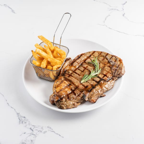 Grilled steak with rosemary sprigs and a side of golden french fries in a metal basket.