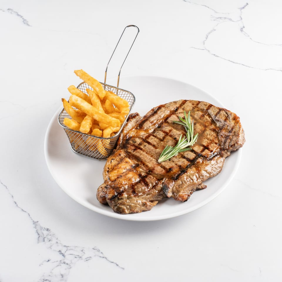 Grilled steak with rosemary sprigs and a side of golden french fries in a metal basket.