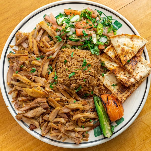 Palestinian chicken shawarma plate with rice, salad, pita bread, grilled tomato, and jalapeño.