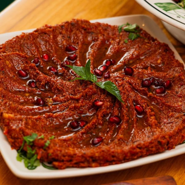 Palestinian muhammara, a red pepper dip, garnished with pomegranate seeds and mint on a white plate.